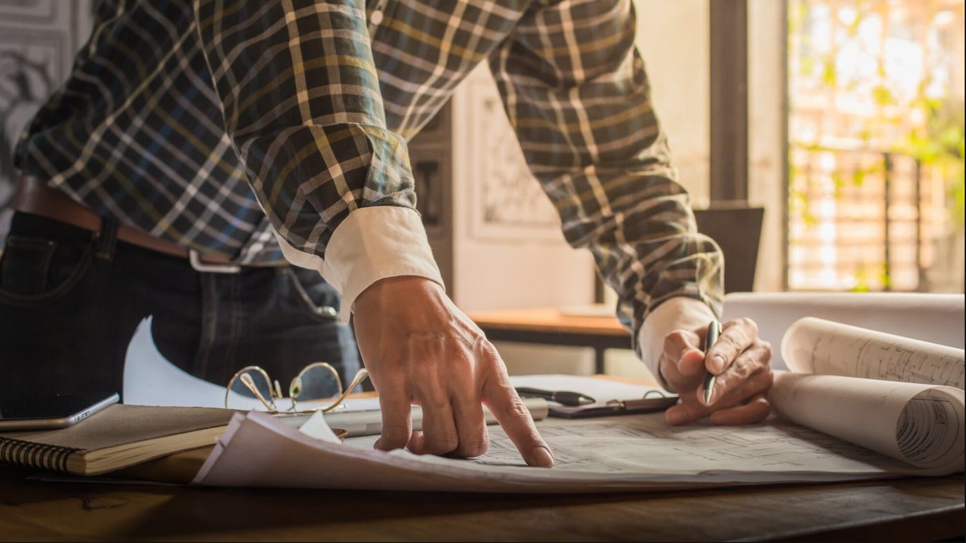 Architecte NA'BUILD annotant des plans sur sa table de travail
