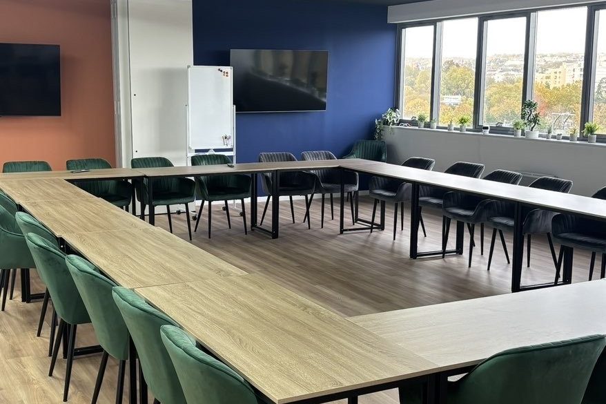 Salle de réunion aménagée avec grande table et chaises vertes