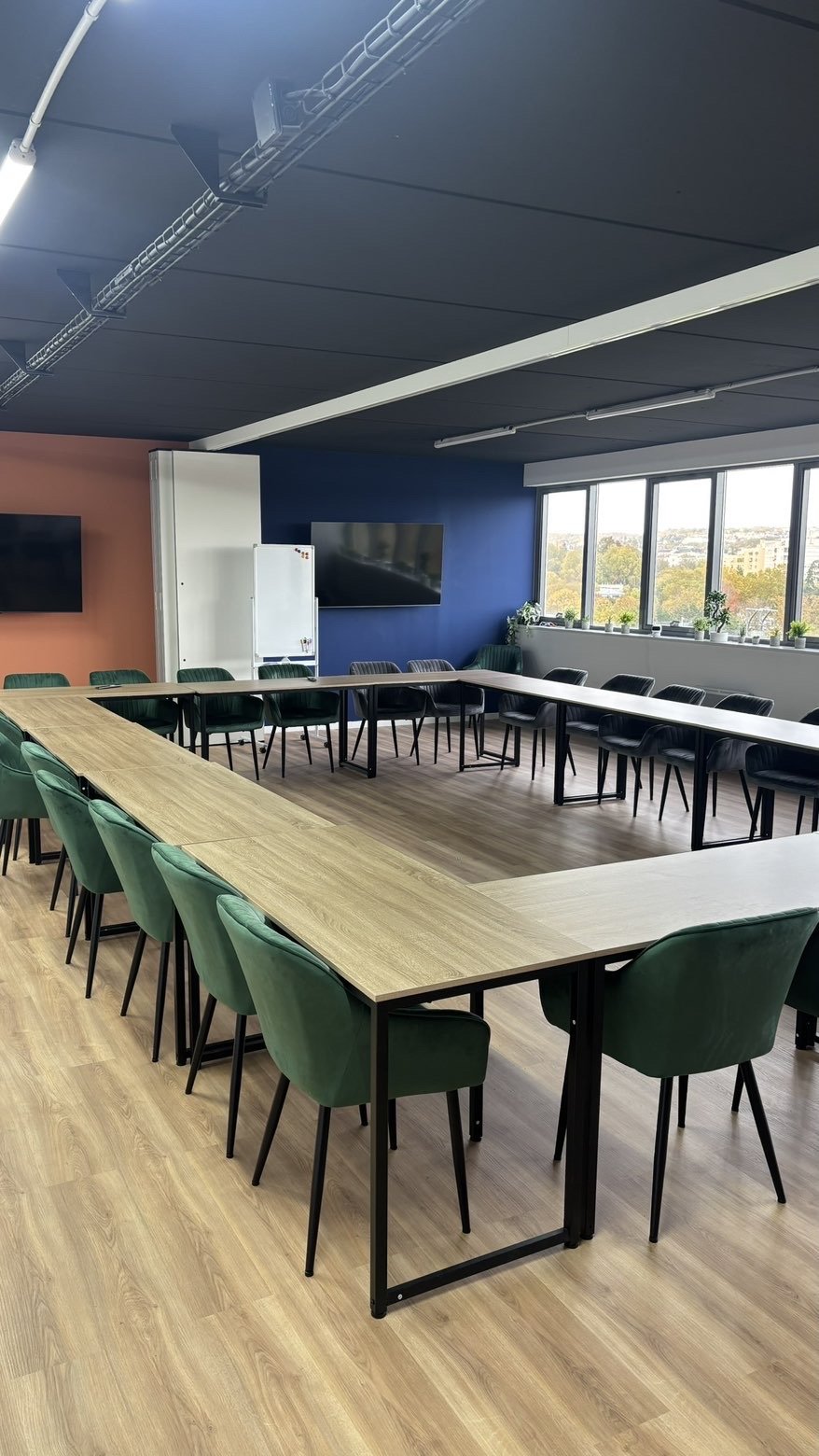Salle de réunion aménagée avec grande table et chaises vertes